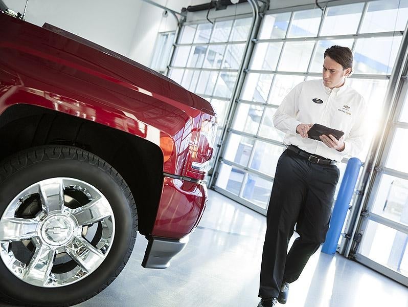 Technician inspecting a red Chevrolet pickup truck in a dealership service area.
