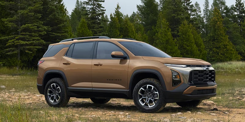 A bronze Chevrolet Equinox SUV parked on a dirt trail beside a forest.